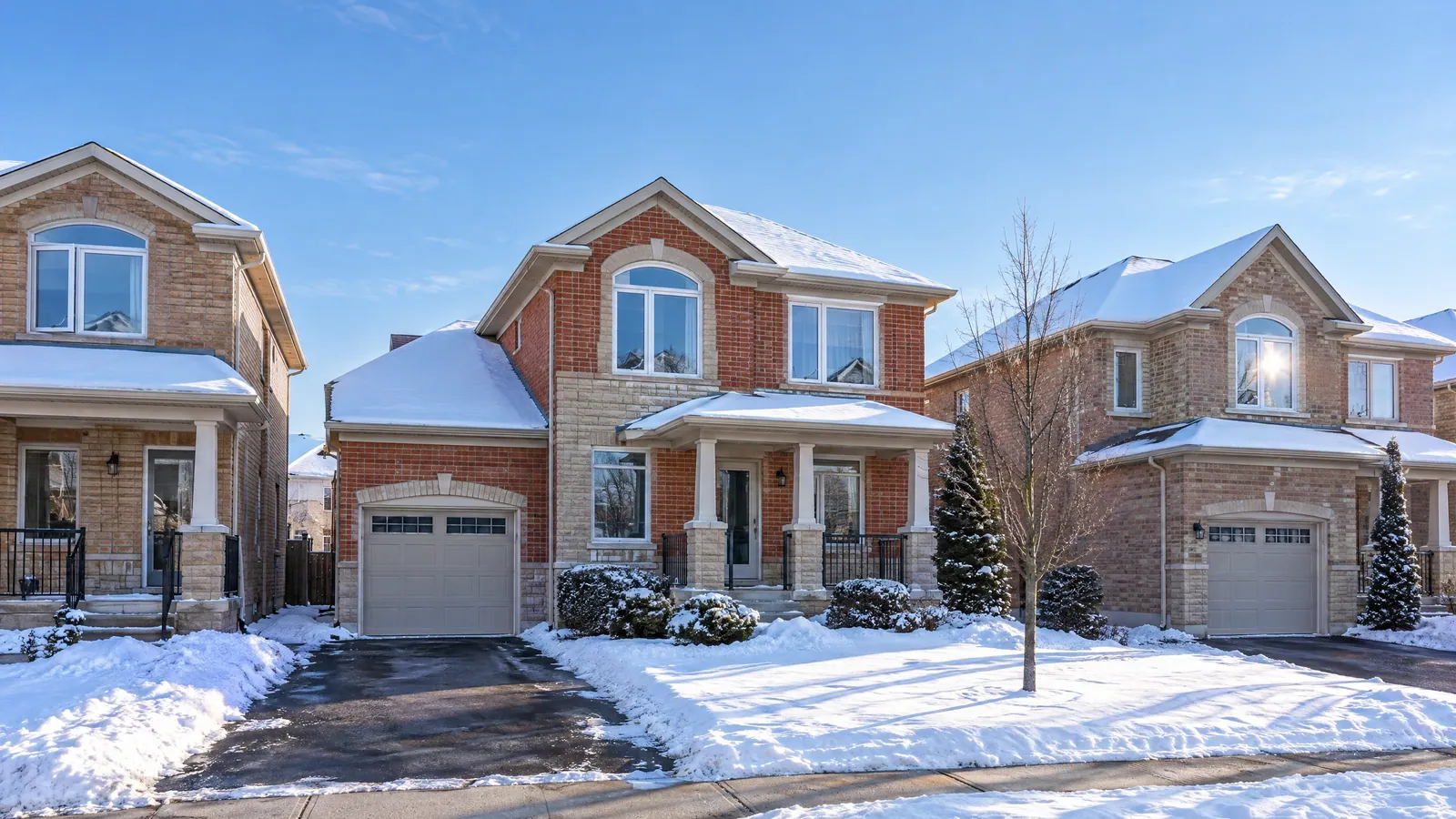 Street of two-storey brick semi-detached and detached houses with white vinyl casement windows, arched upper windows and snow-covered front yards on a sunny winter day