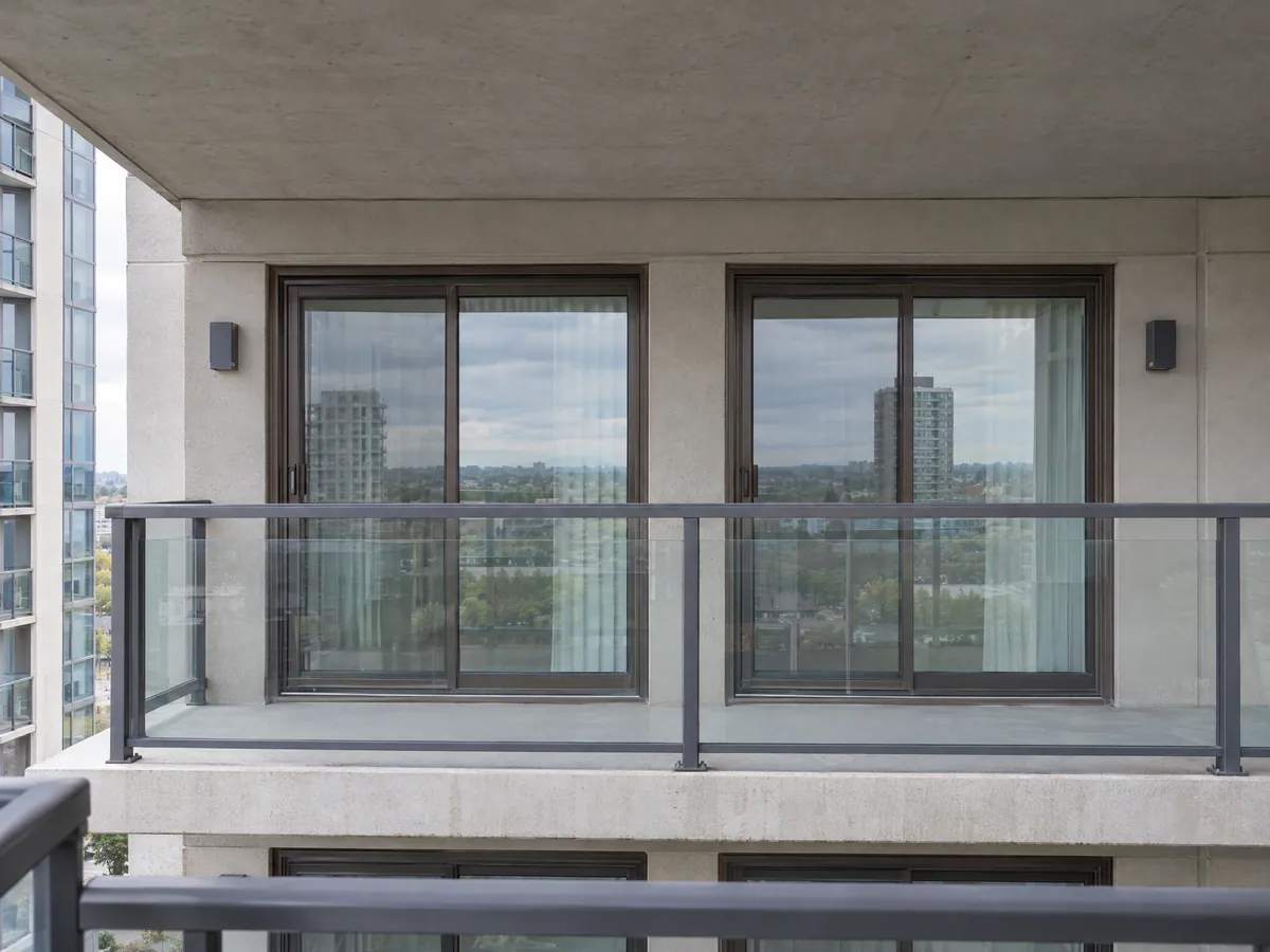 Two neighbouring condo balcony sliding doors with matching bronze frames behind a glass balcony guard, one of them newly replaced