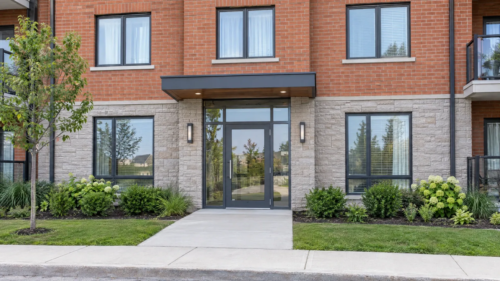 Entrance of a newer low-rise apartment building with a black-framed glass door, glass sidelights and matching black-framed windows in brick and stone