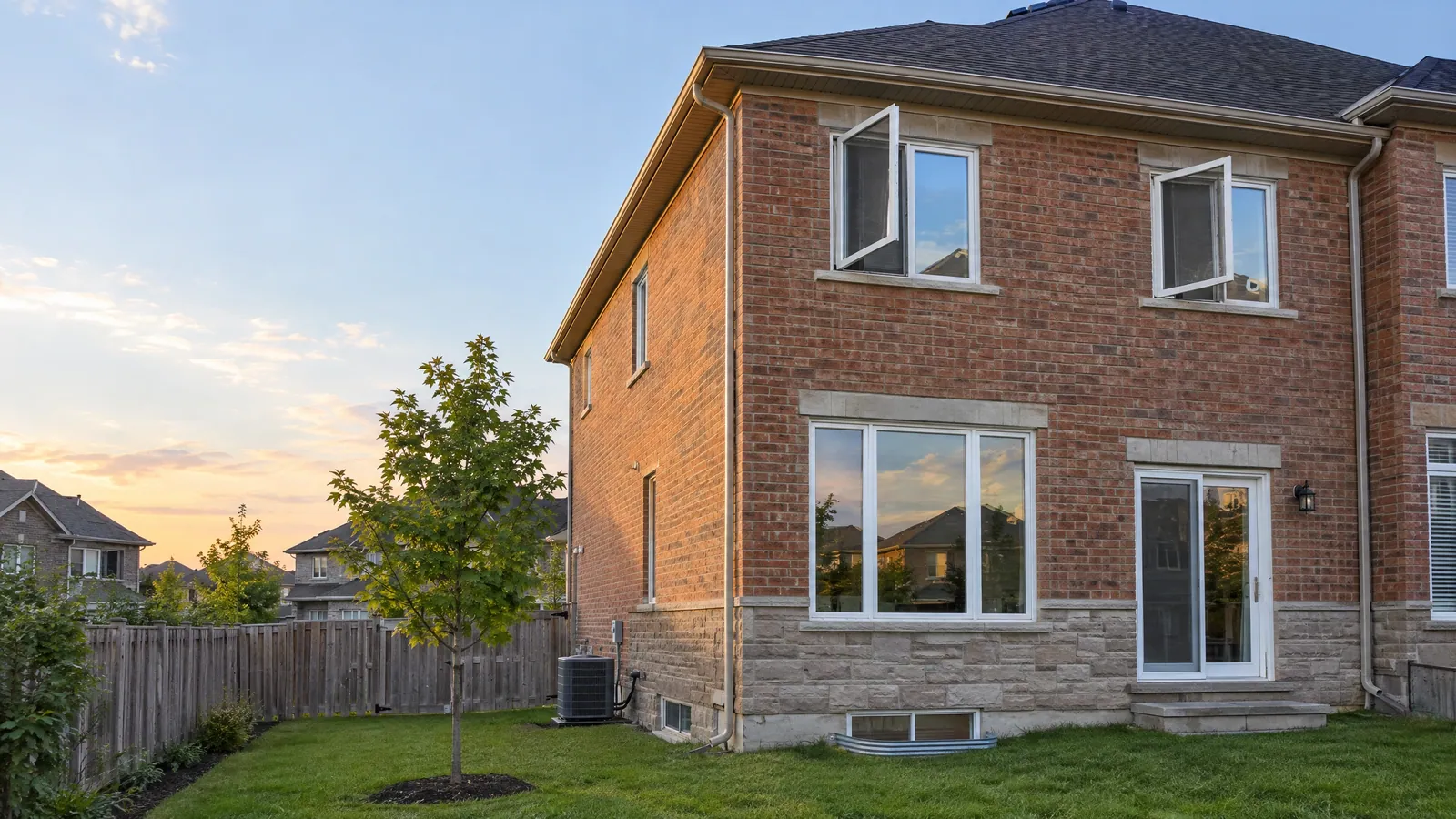 Brick semi-detached house at sunset with two upstairs casement windows cranked open outward